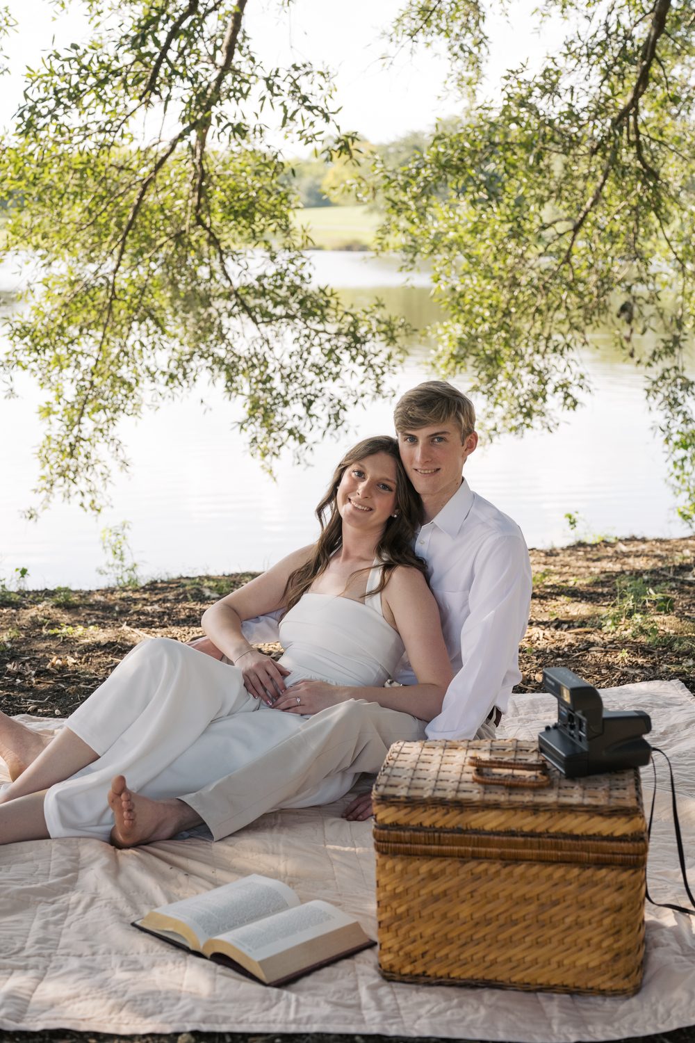 Colton and Ashlyn on a picnic blanket by the water with a wicker basket.