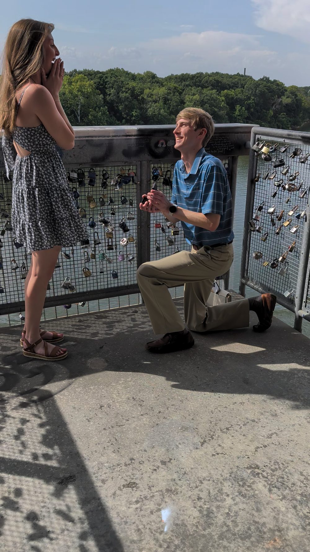Colton on one knee proposing to Ashlyn at the lock bridge on the Montgomery riverfront.
