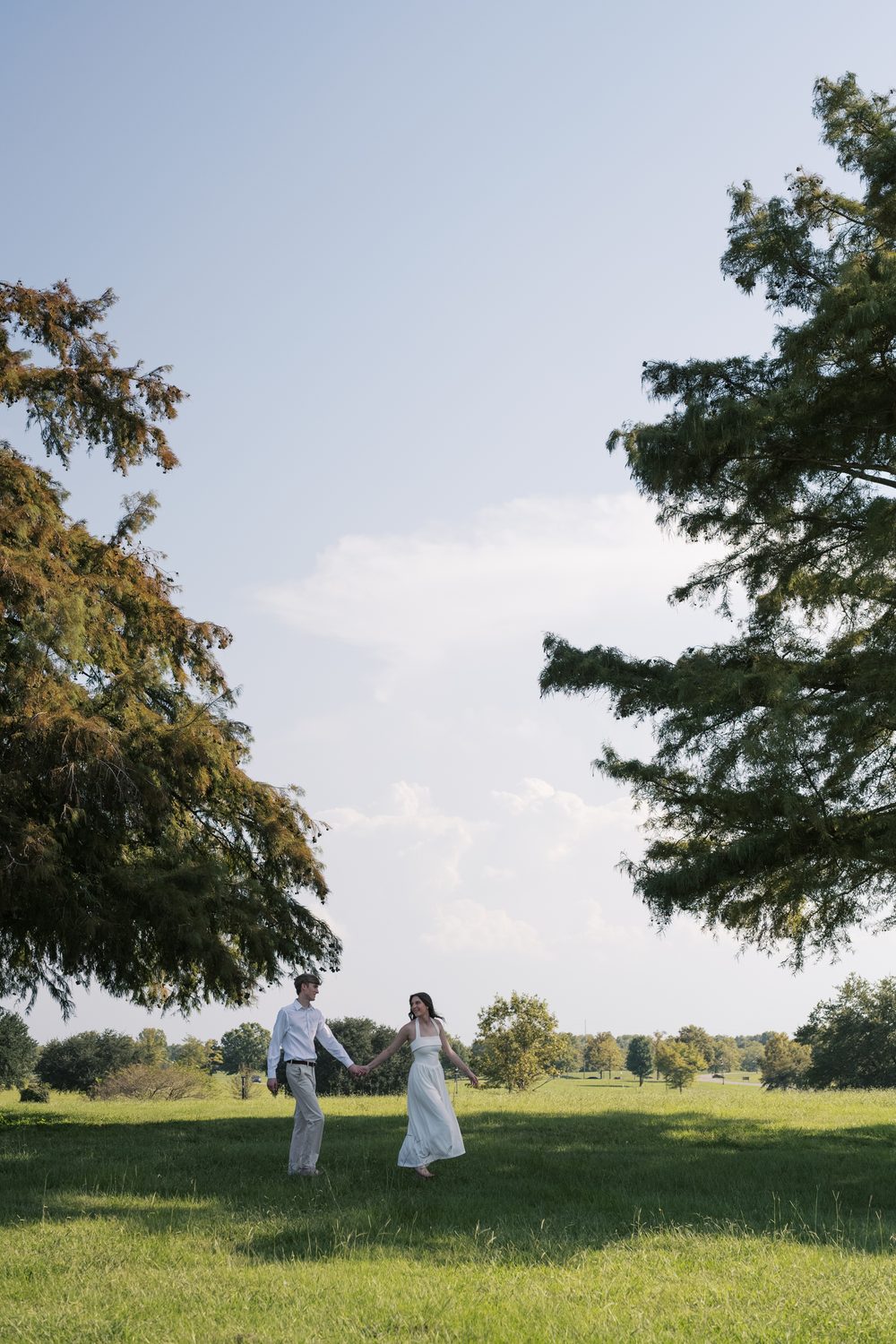 Colton and Ashlyn walking together beneath tall cypress trees.